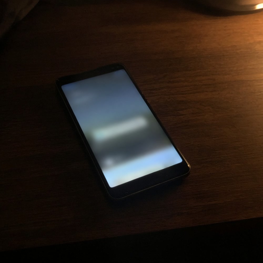 Smartphone lying face up on a clean wooden table next to a ceramic cup