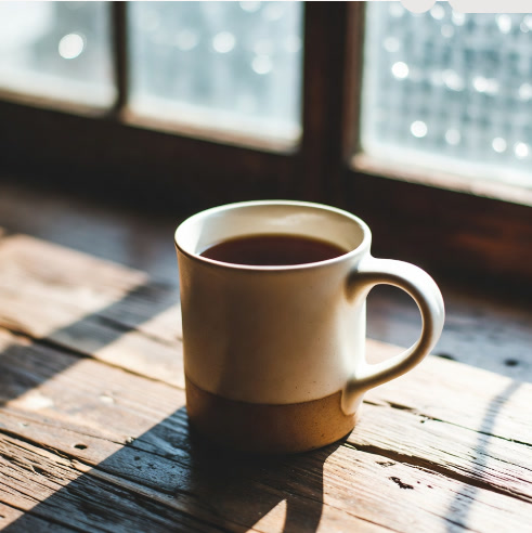 Hot ceramic mug of tea sitting on a wooden table in soft morning light