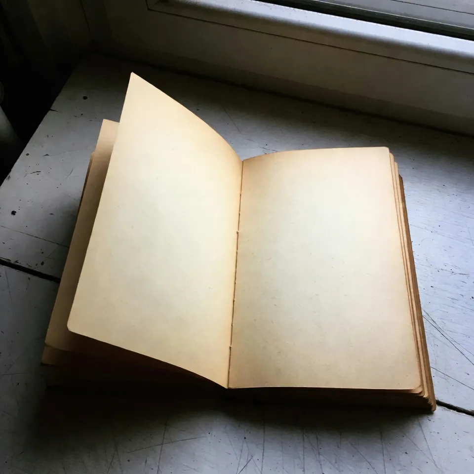 An open book resting on a wooden table under soft diagonal sunlight