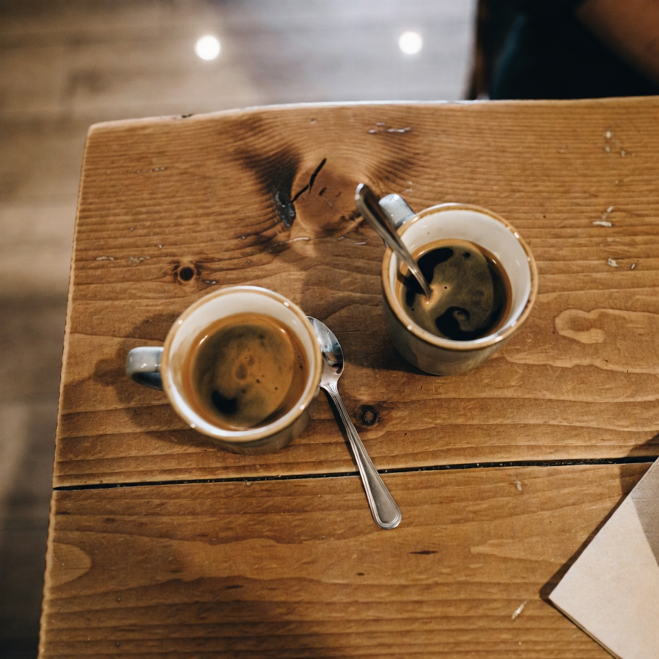 Two coffee cups sitting on a wooden cafe table with warm indoor lighting